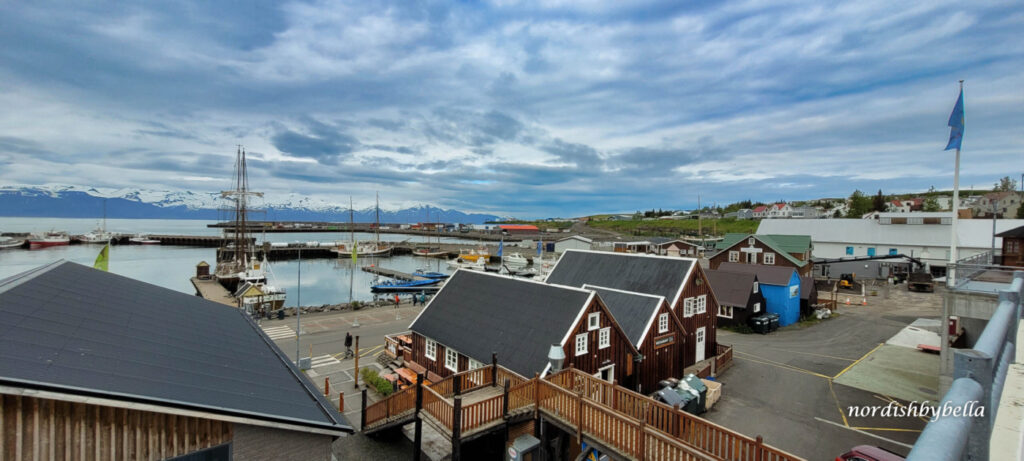 Boote im Hafen der Stadt Húsavík. Im Hintergrund sind schneebedeckte Berge.