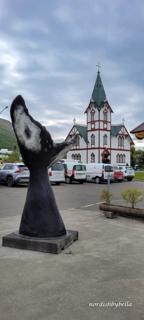 Künstliche Haifischflosse als Symbol für Húsavik und im Hintergrund eine isländische Kirche, die Húsavíkurkirkja