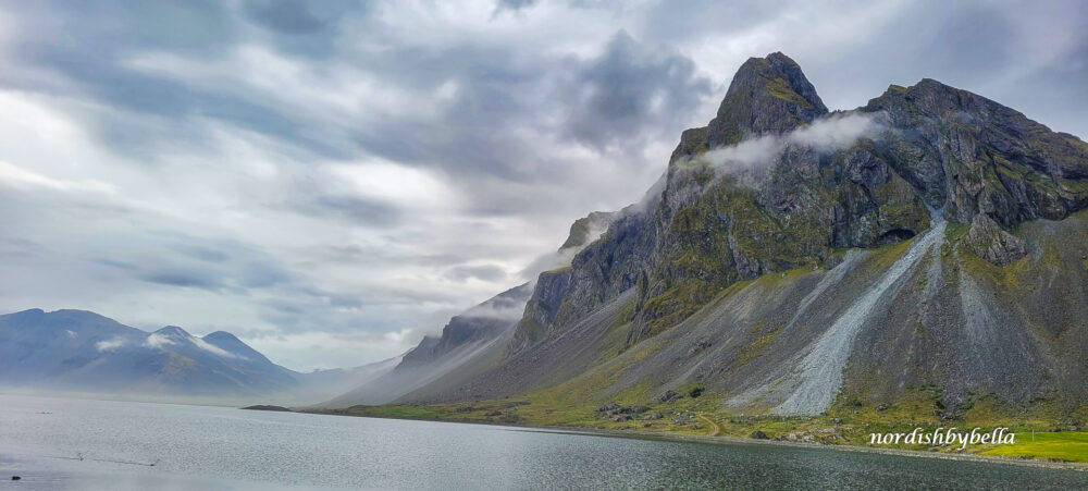 Wasser mit steilen Bergen am Rand, an denen Wolken hängen